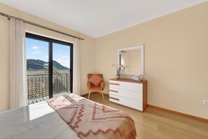 Une chambre à coucher avec un lit, une chaise, une commode et une grande fenêtre.