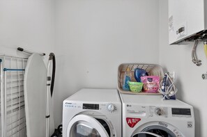 A laundry area with a washing machine, a drying rack, and a basket containing laundry supplies. - Villa Bella - Mountain views & Outdoor living (Machico)