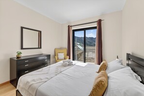 A bedroom with a bed, a dresser, a chair, and a view of mountains through a window. - Villa Bella - Mountain views & Outdoor living (Machico)
