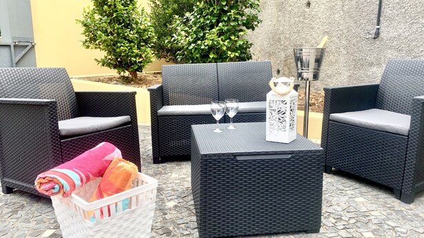 A patio area with wicker furniture, a white basket with towels, and a table with two glasses. - Villa Bella (Machico)