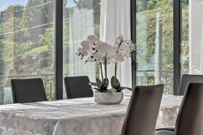 A dining table with a white tablecloth, a white vase with orchids, and black chairs. - Villa Bella - Mountain views & Outdoor living (Machico)