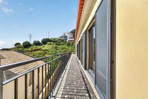 A narrow outdoor corridor with a metal railing, leading to a building with a closed shuttered door. - Villa Bella - Mountain views & Outdoor living (Machico)