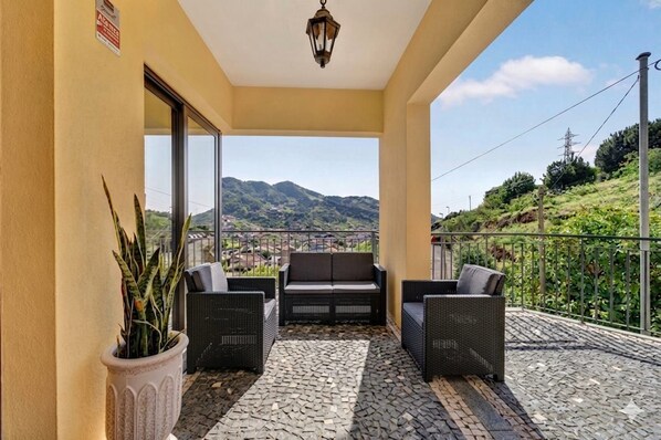 A balcony with wicker furniture, a potted plant, and a view of mountains. - Villa Bella - Mountain views & Outdoor living (Machico)