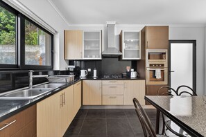 A modern kitchen with a black countertop, stainless steel sink, wooden cabinets, and a built-in oven. - Villa Bella - Mountain views & Outdoor living (Machico)