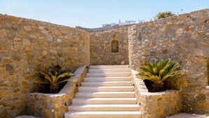 Un escalier en pierre, dont les marches mènent à un niveau supérieur, est bordé de murs en pierre et agrémenté de plantes en pot.