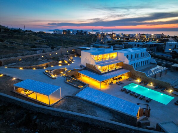 A modern villa with a pool, solar panels, and a scenic sunset view.