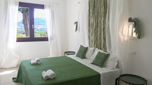 A bedroom with a bed, pillows, a nightstand, a window with curtains, and a wall-mounted light fixture.
