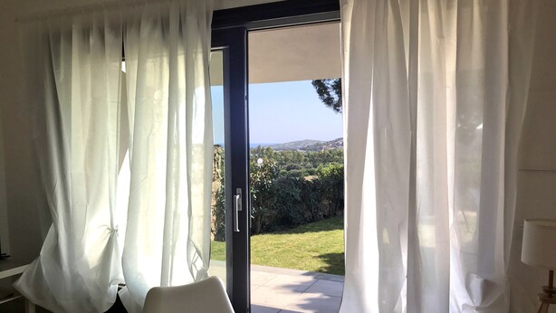 A room with a sliding glass door leading to a patio with a view of greenery and hills.