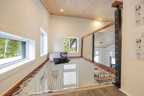 Quarto com cama em rede, janelas amplas e vista para árvores.