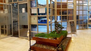 A modern interior with a glass door entrance, a wooden planter with greenery, and a signboard.