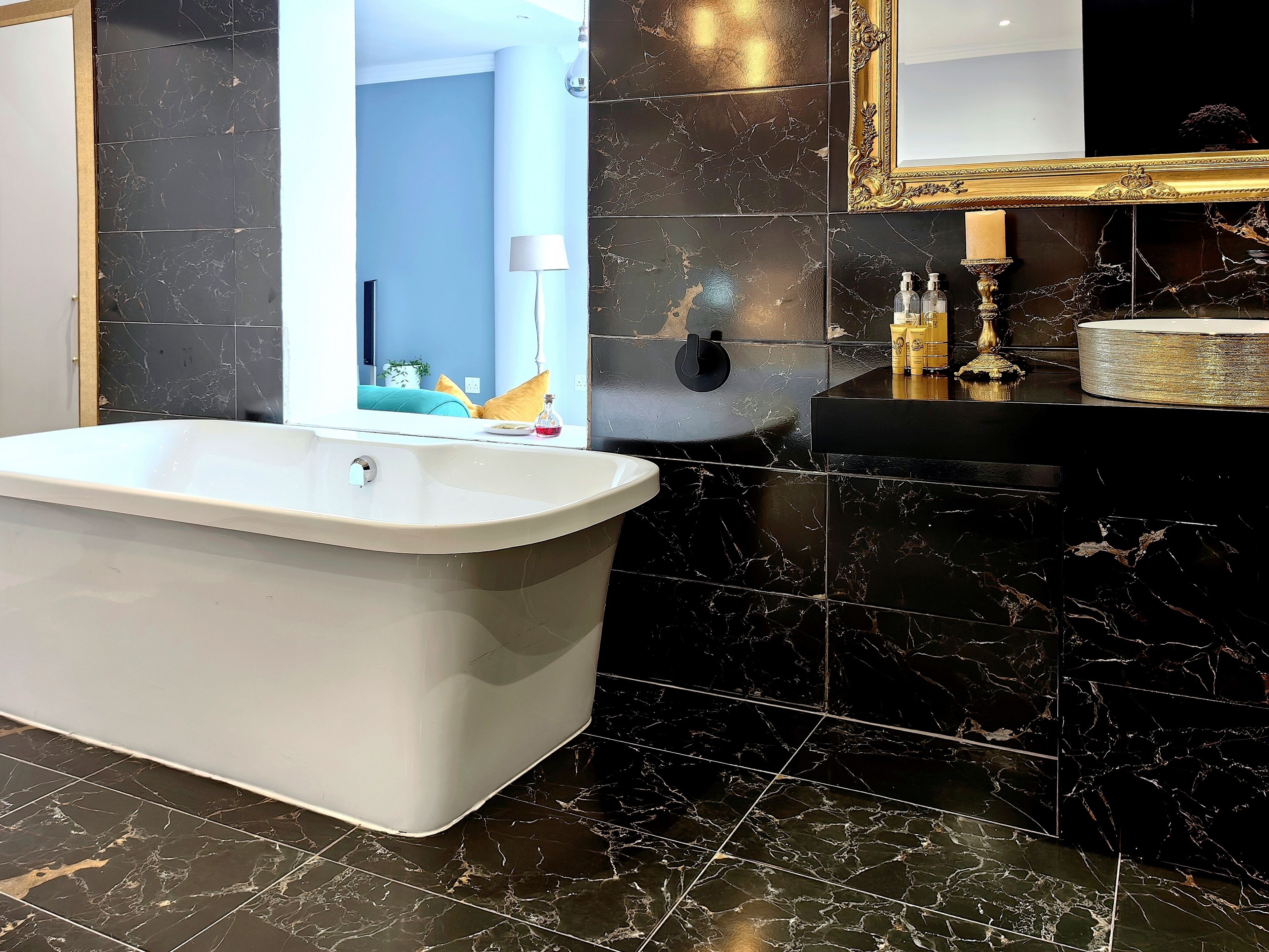 A modern bathroom with a freestanding bathtub, a vanity with a mirror, and black marble tiles.