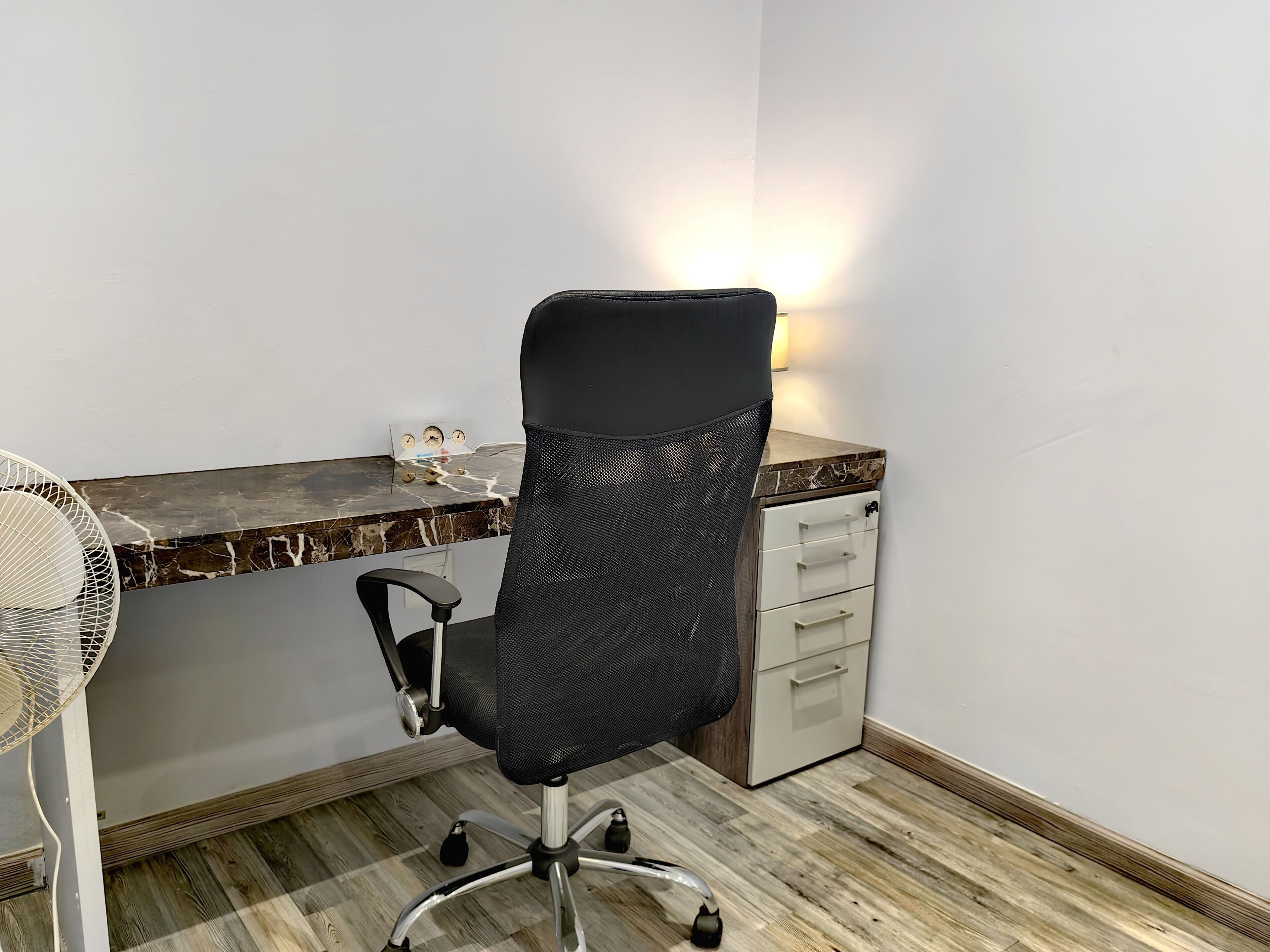A small office space with a desk, chair, and a fan.