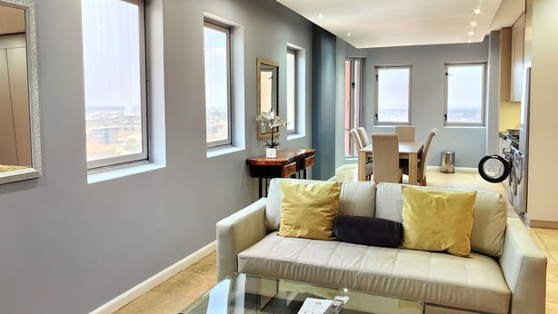 A modern living room with a sofa, a glass coffee table, and a dining area with chairs and a table.