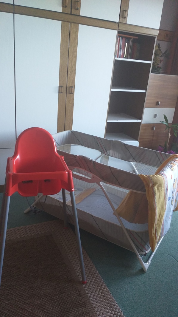 Una habitación con literas, una silla roja, una estantería y una planta pequeña.