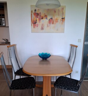Un coin repas avec une table ronde, quatre chaises, un bol bleu et un tableau accroché au mur.