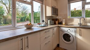 A modern kitchen with white cabinets, a built-in washing machine, a microwave, and a window with a view of greenery.
