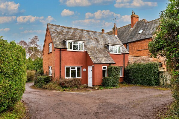 A two-story house with a red brick exterior, a sloped roof, and a front entrance. - Glebe Cottage (Wellington)