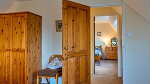 A room with a wooden wardrobe, a chair with a cushion, and a bed with a blue and white patterned blanket.