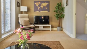 A living room with a beige sofa, a flat-screen TV, a world map on the wall, a potted plant, and a small table with flowers.