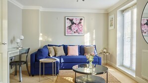 A living room with a blue sofa, a glass coffee table, and a framed floral artwork on the wall.