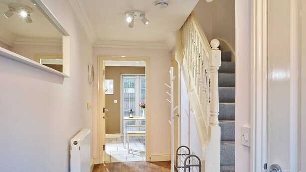 A hallway with a wooden floor, a radiator, a mirror, and a staircase with a banister.