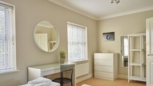 A bedroom with two beds, a desk, a chair, a radiator, a wardrobe, and a window with blinds.