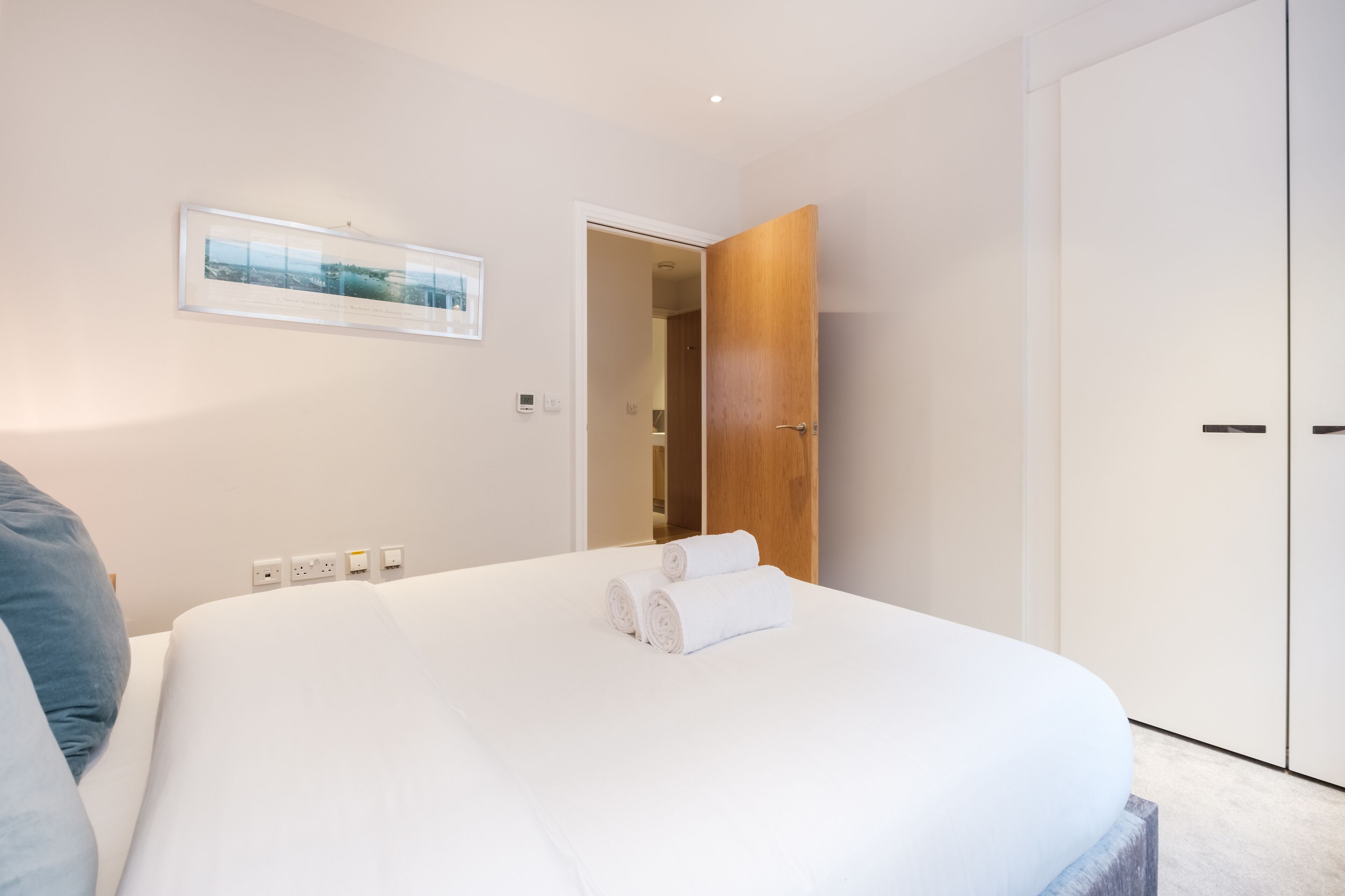A modern hotel room with a neatly made bed, a wooden wardrobe, and a framed picture on the wall.