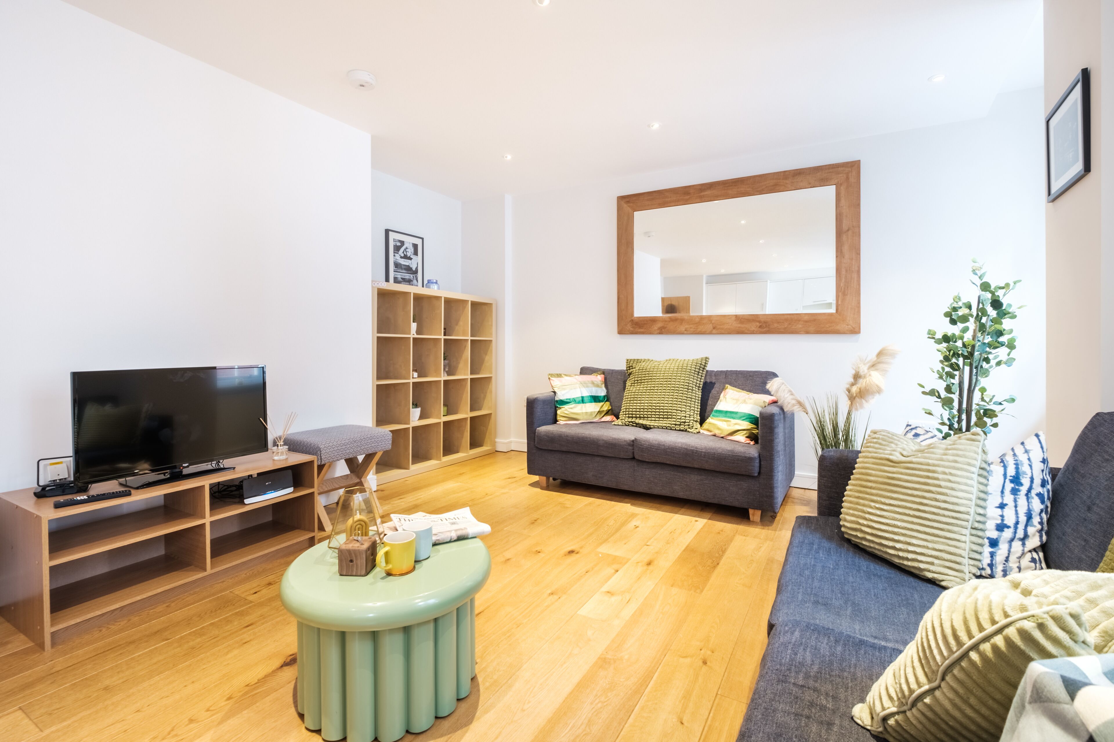 Un salon moderne avec un téléviseur à écran plat, un meuble de rangement en bois, un canapé gris et un grand miroir.