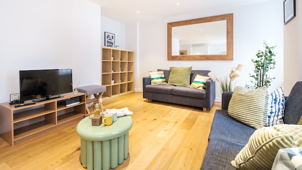 Un salon moderne avec un téléviseur à écran plat, un meuble de rangement en bois, un canapé gris et un grand miroir.
