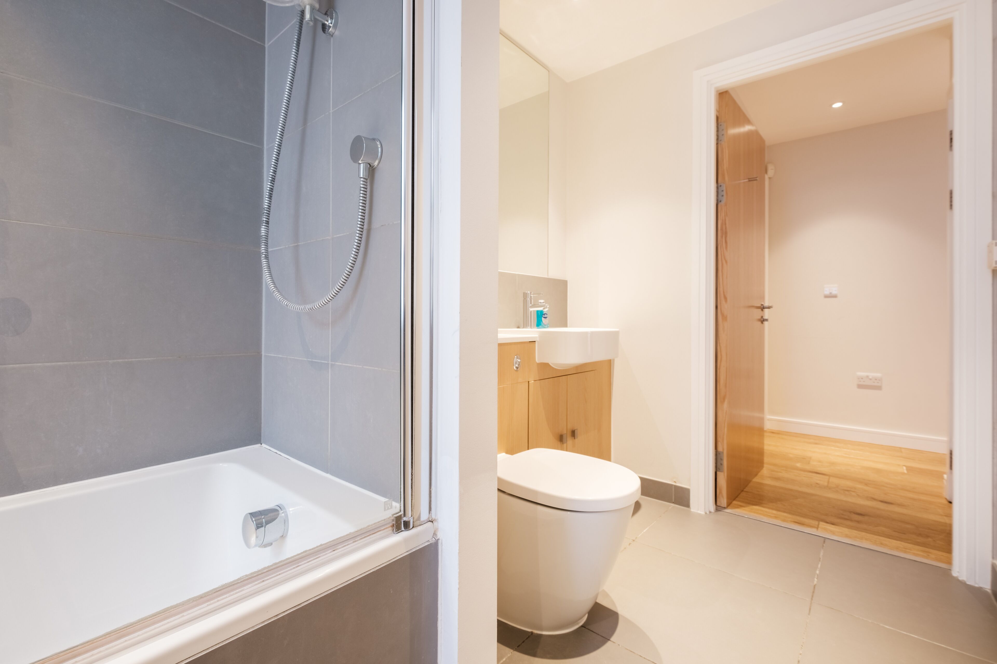 A modern bathroom with a glass-enclosed shower, a white toilet, and a wooden floor.