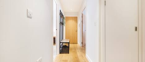 A hallway with wooden flooring, white walls, and a bench.