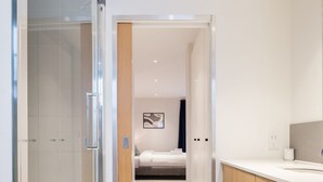 Habitació d'hotel moderna amb dutxa de vidre, tocador de fusta i llit amb vista.