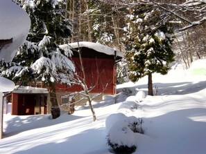 A snow-covered landscape with a red building, possibly a barn, surrounded by trees and snow. - Cozy vacation home surrounded by greenery (Frauenstein)