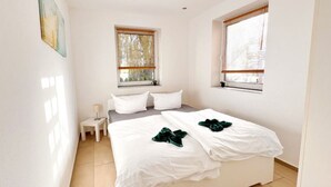 A bedroom with two beds, a small bedside table, and two windows with blinds. - Apartment "Just Live" at the mill pond (Wismar)