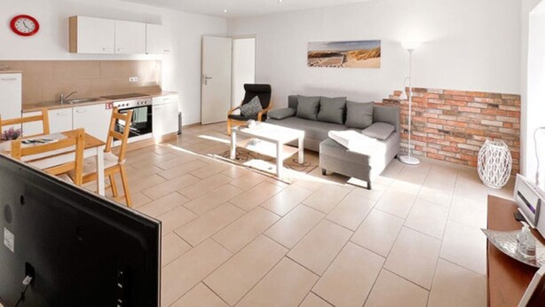 A modern living room with a sofa, coffee table, and a dining area with chairs and a table. - Apartment "Just Live" at the mill pond (Wismar)