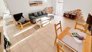 A modern living room with a grey sofa, a wooden chair, a coffee table, and a TV stand with a brick accent wall. - Apartment "Just Live" at the mill pond (Wismar)