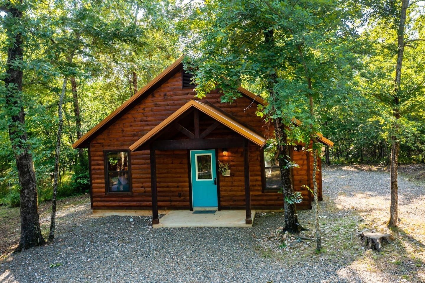 Une cabane en bois dotée d’un porche, entourée d’arbres.