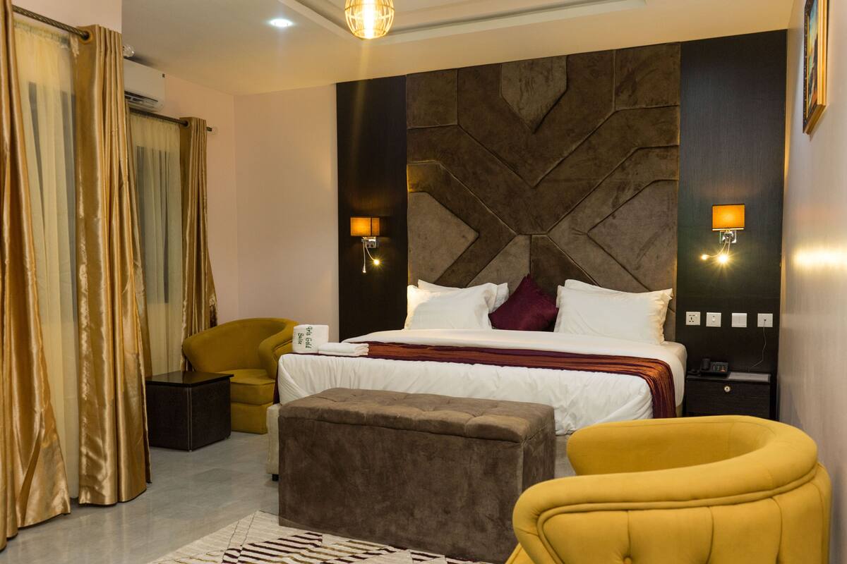 A modern hotel room with a large bed, a sofa, a small table, and a decorative wall panel.