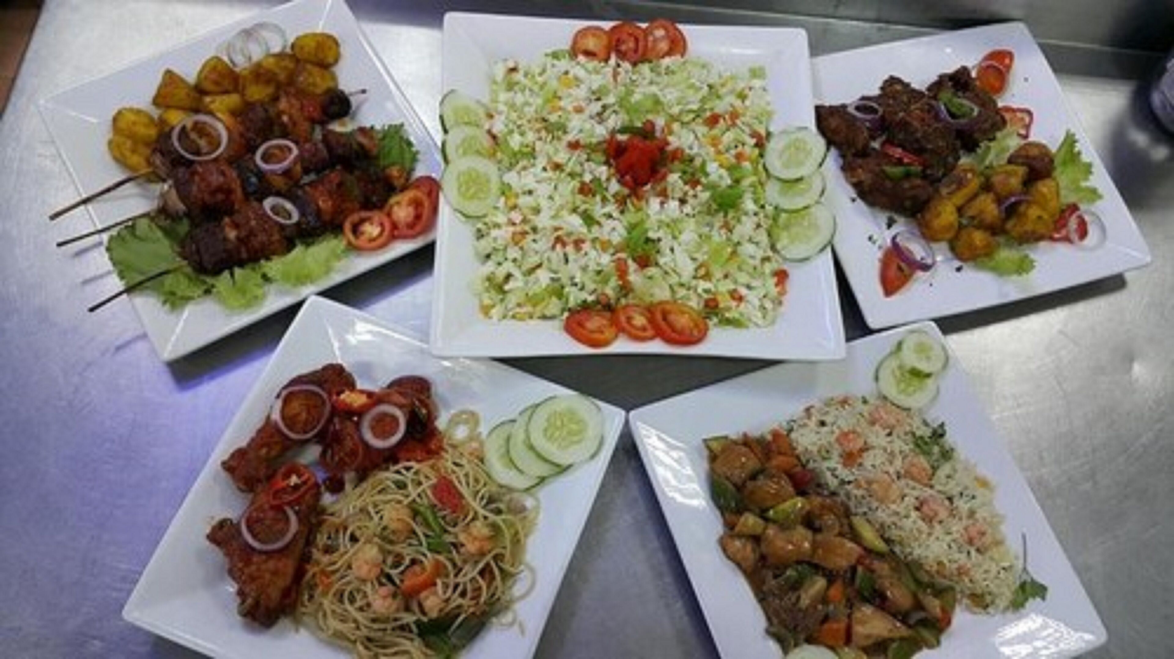 A table with various dishes including skewered meats, a salad, and stir-fried vegetables.
