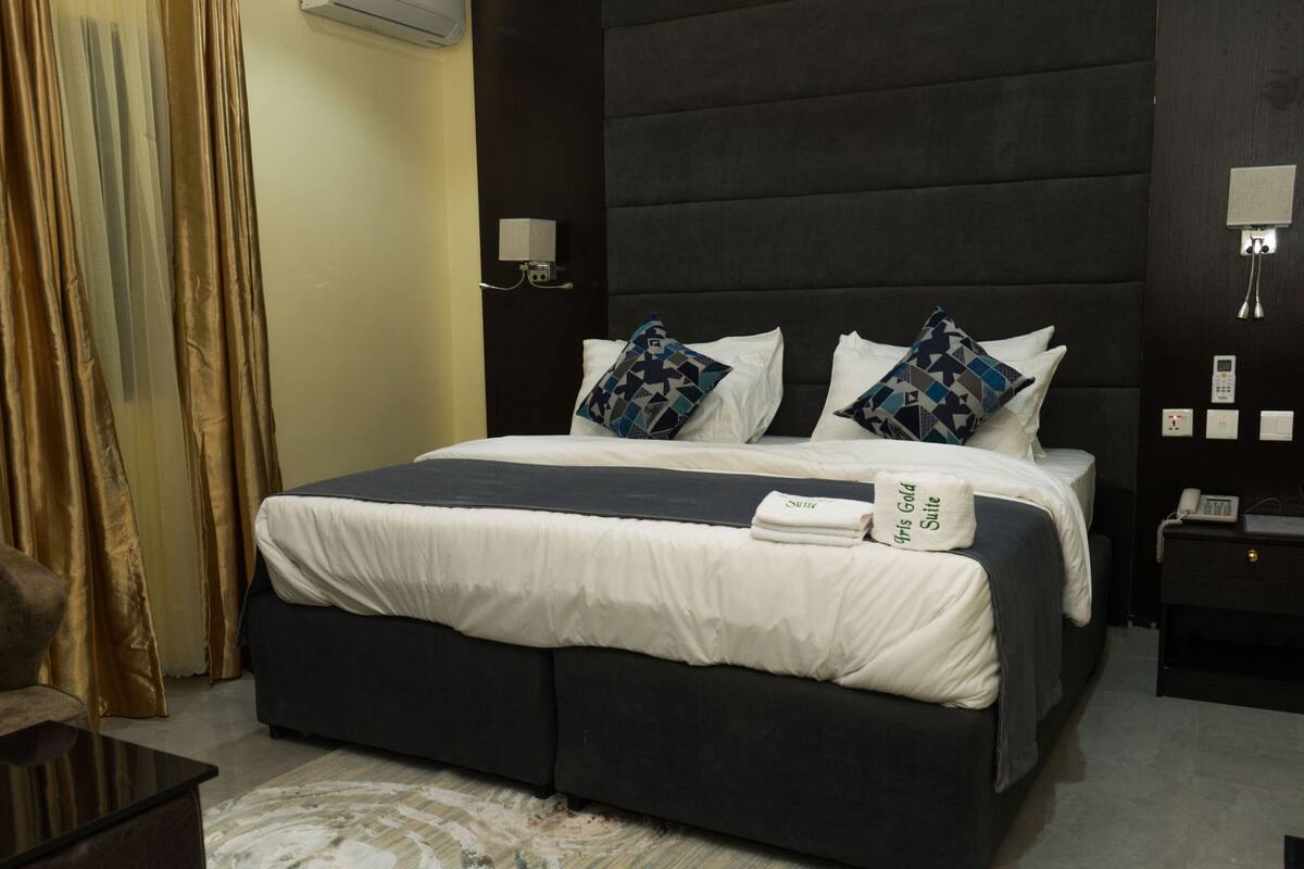 A hotel room with a large bed, two pillows, a bedside table with a lamp, and a chair.