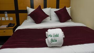 A hotel room with a bed, two pillows, a bedside table with a phone, and a towel with "IRIS GOLD SUITE" embroidered on it.