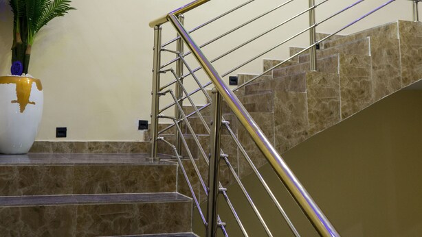 A staircase with a metal railing, a painting of a mountain landscape, and a potted plant. - Iris Gold Suite (Ibadan)