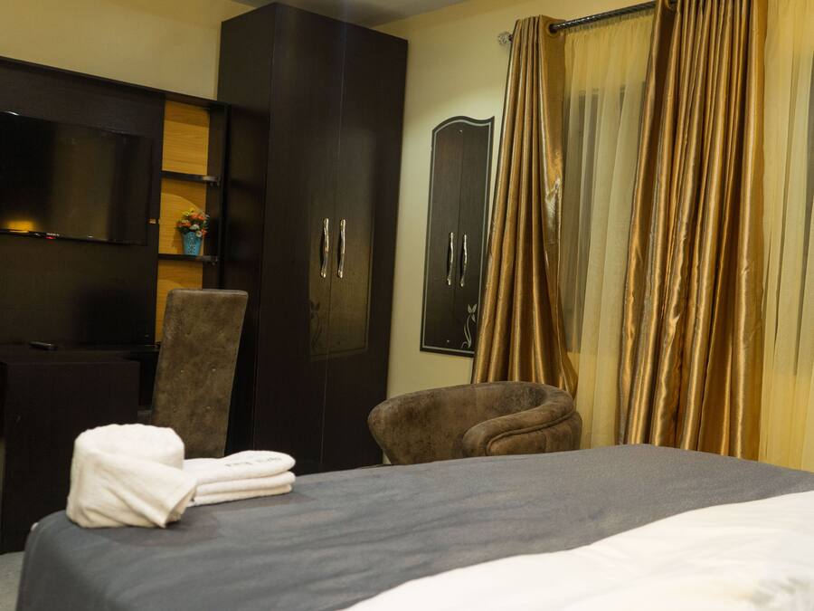 A hotel room with a bed, a TV mounted on the wall, a wardrobe, a chair, and a curtain.