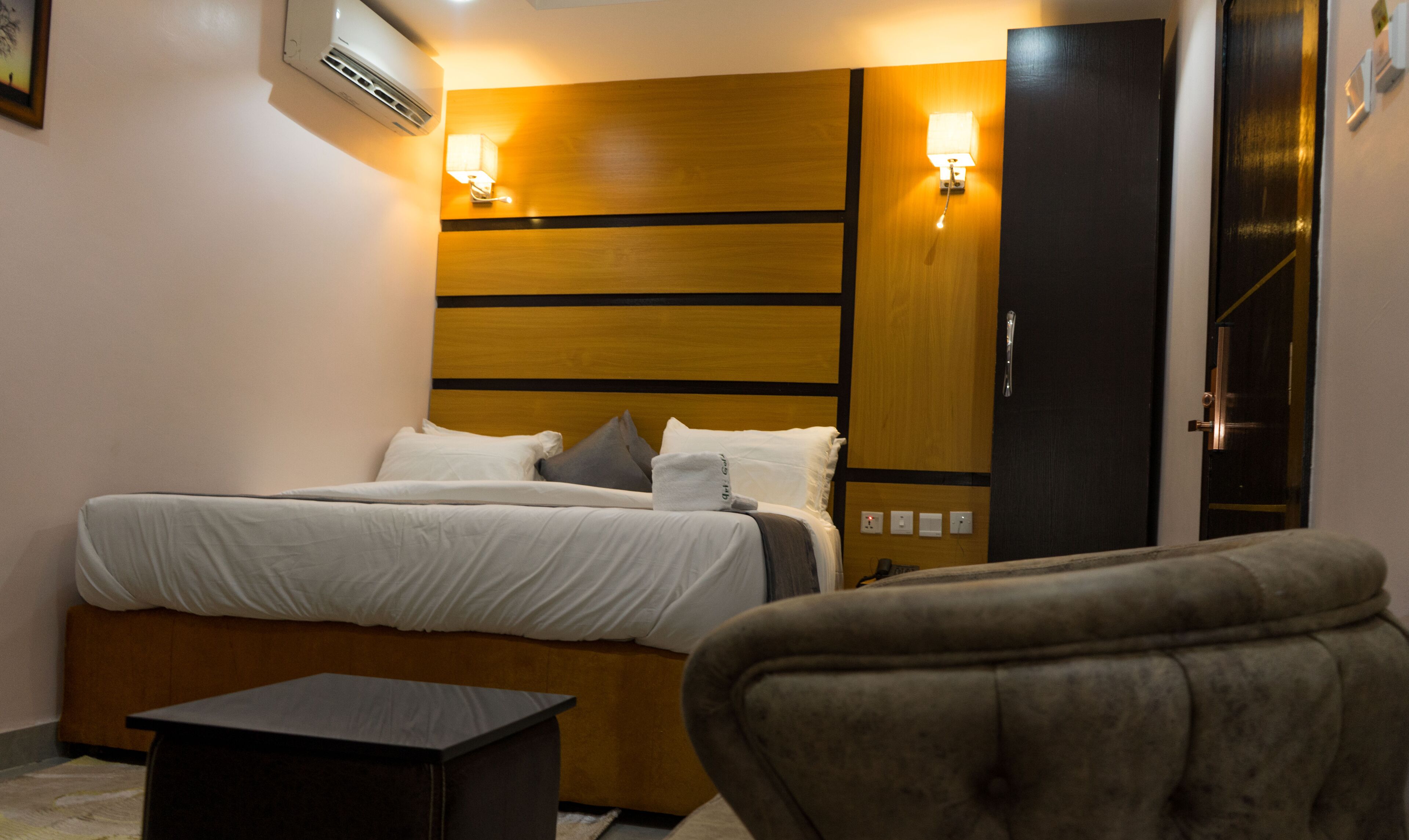 Een hotelkamer met een bed, nachtlampjes, een klein tafeltje en een kledingkast.