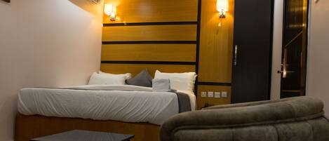 A hotel room with a bed, bedside lamps, a small table, and a wardrobe.