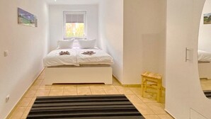 Une chambre à coucher avec un lit, une fenêtre, un petit tabouret et une armoire.