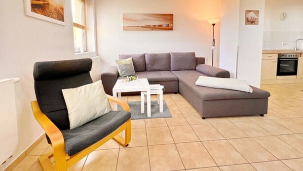 Un salon moderne avec un canapé d’angle, un fauteuil en bois et une petite table blanche.