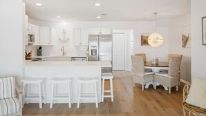 A modern kitchen with white cabinetry, a central island with stools, and a dining area with wicker chairs.