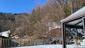 A snow-covered landscape with a wooden fence, a glass building with metal furniture, and a mountainous backdrop. - Family mountain chalet, Close to the Brasses ski slopes (Saint-Jeoire)