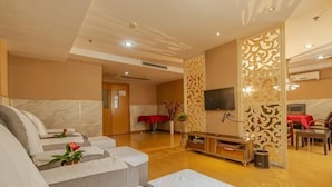 Quarto de hotel moderno com sofá, TV, área de refeições e painel decorativo na parede.